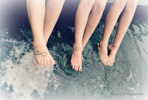 Three good friends dangle bare feet in the water.