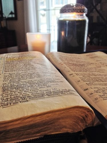 Open bible on table and a burning candle illustrate post on how to meditate on God's Word.