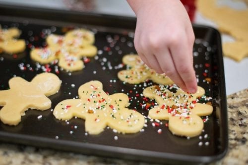Child's hand decorating sugar cookies as example of a meaningful christmas tradition.