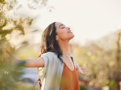 Grateful woman looks at the sun with arms widespread.